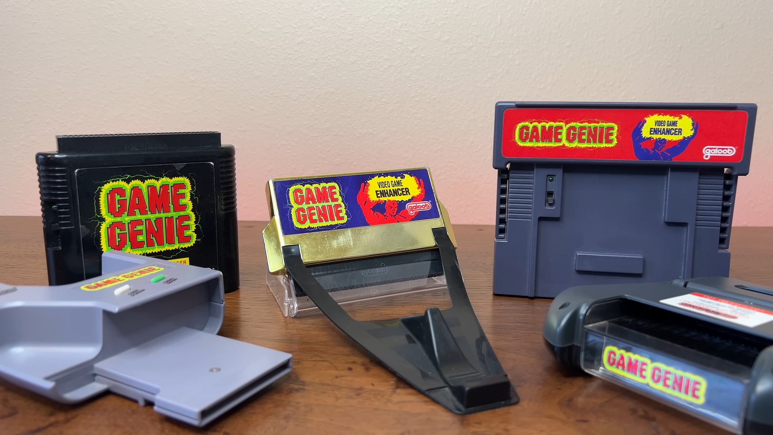 A lineup of Game Genies from left to right: GameBoy, Sega Genesis, NES, SNES and Game Gear. Via gruz, Youtube.