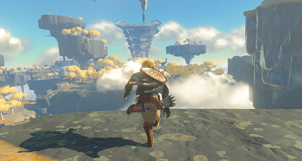 Link runs towards the edge of a cliff, overlooking floating islands with yellow-leafed trees and ruins via The Legend of Zelda: Tears of the Kingdom (2023), Nintendo