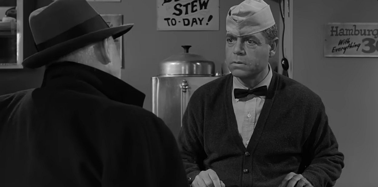 Two disguised aliens speaking at a cafe