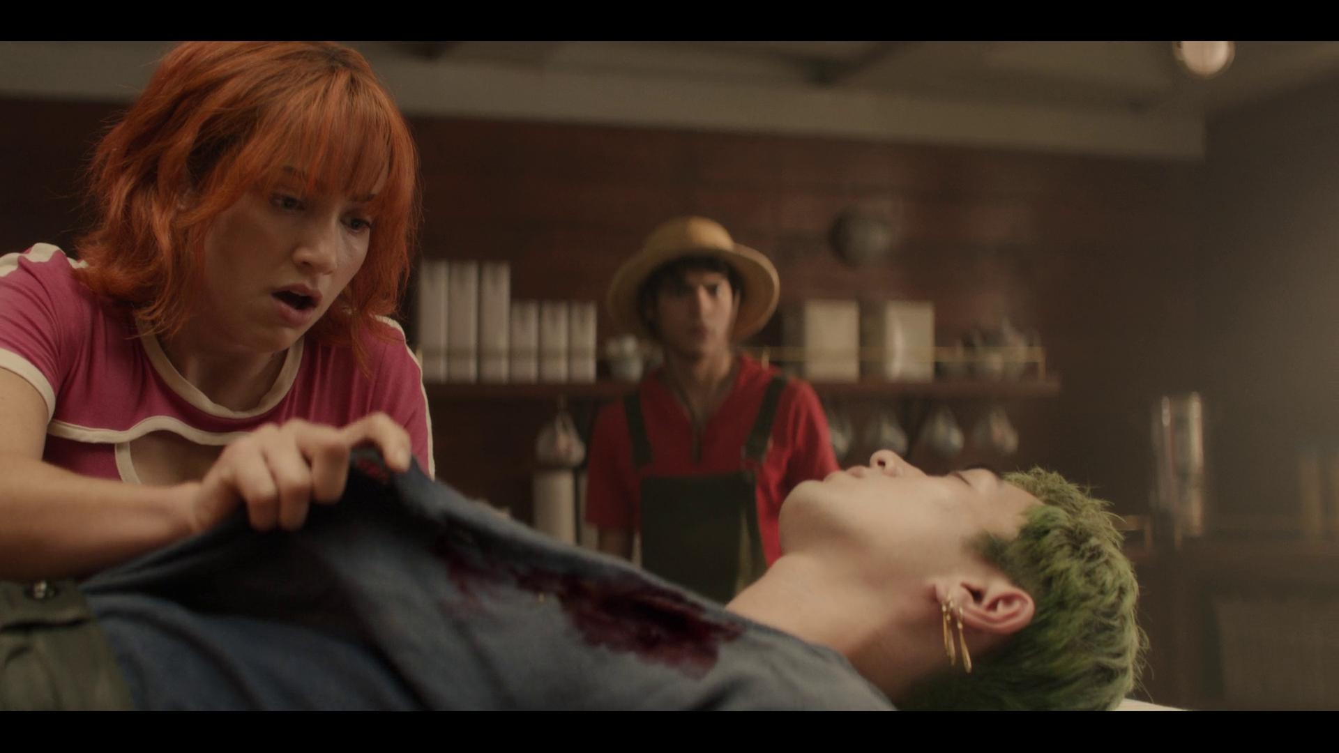 Nami (Emily Rudd) and Luffy (Iñaki Godoy) take stock of Zoro's (Maceknyu) wound in One Piece Season 1 Episode 6 "The Chef and the Chore Boy" (2023), Netflix