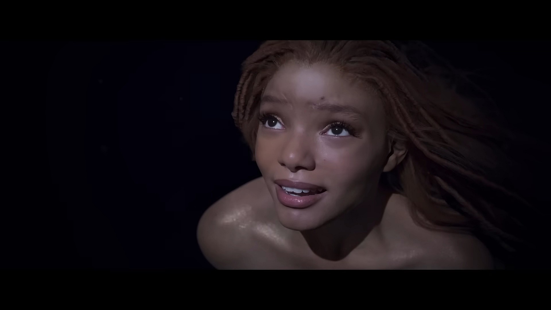 Ariel (Halle Bailey) takes notice of a naval battle happening above the surface in The Little Mermaid (2023), Disney