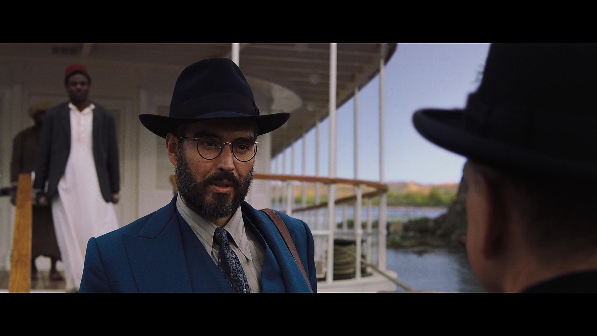 Dr. Windlesham (Russell Brand) thanks Inspector Poirot (Kenneth Branagh) for his help in solving the titular murder in Death on the Nile (2022), 20th Century Studios