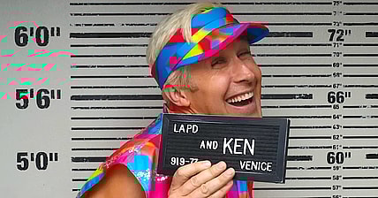 Ken (Ryan Gosling) smiles as he has his mugshot taken in Barbie (2023), Warner Bros. Pictures