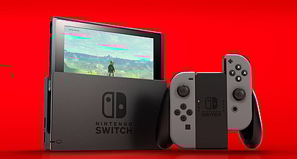A Nintendo Switch with grey Joy-Cons on a red background. The Legend of Zelda: Breath of the Wild can be seen on the screen via Nintendo