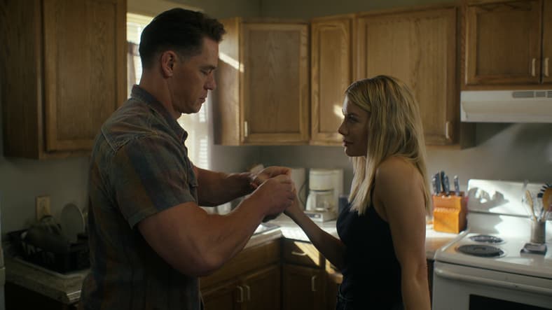 Christopher Smith (John Cena) helps Emilia Harcourt (Jennifer Holland) bandage her bloody knuckles in Peacemaker Season 2 Episode 1 "The Ties That Grind" (2025), DC Studios