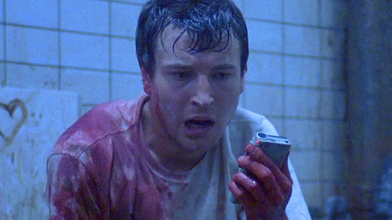 Adam (Leigh Whannell) discovers a surprise Jigsaw (Tobin Bell) recording on Dr. Gordon's (Cary Elwes) corpse in Saw (2004), Lionsgate Films