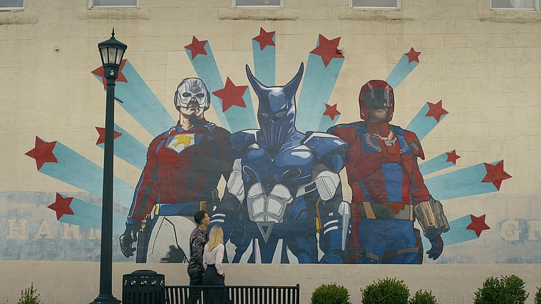 Peacemaker (John Cena) and Harcourt (Jennifer Holland) take in a mural of the Top Trio in Peacemaker Season 2 Episode 3 "Another Rick Up My Sleeve" (2025), DC Studios