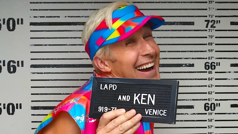 Ken (Ryan Gosling) smiles as he has his mugshot taken in Barbie (2023), Warner Bros. Pictures
