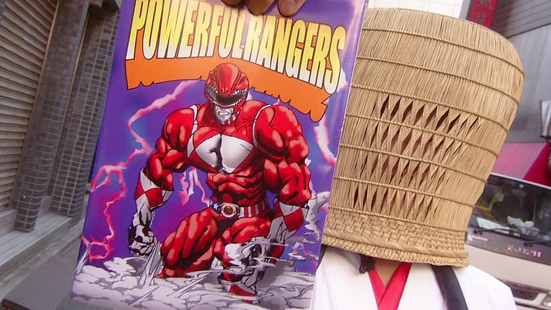 A mysterious priest (Katsuyuki Konishi) offers AkibaRed (Masato Wada) a free 'Powerful Rangers' bible in Unofficial Sentai Akibaranger Season 2, Episode 5 "Delusional Imports" (2013), Toei Co. Ltd.