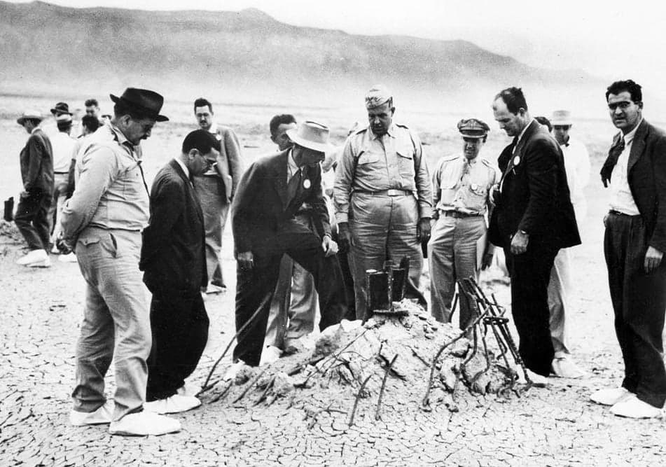  Rare government image of J. Robert Oppenheimer (in light colored hat with foot on tower rubble), General Leslie Groves (large man in military dress to Oppenheimer's left), and others at the ground zero site of the Trinity test after the bombing of Hiroshima and Nagasaki (some time after the actual test) via  United States Army Signal Corps, Wikimedia Commons