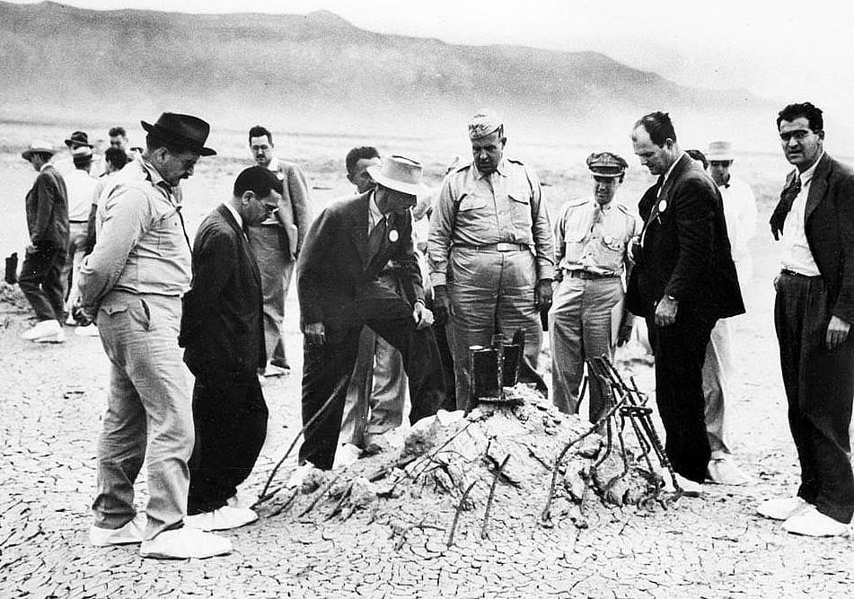  Rare government image of J. Robert Oppenheimer (in light colored hat with foot on tower rubble), General Leslie Groves (large man in military dress to Oppenheimer's left), and others at the ground zero site of the Trinity test after the bombing of Hiroshima and Nagasaki (some time after the actual test) via  United States Army Signal Corps, Wikimedia Commons