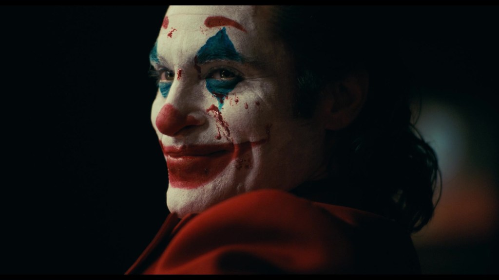 Arthur (Joaquin Phoenix) hits Murray (Robert DeNiro) with the punchline of his best joke in Joker (2019), Warner Bros. Pictures