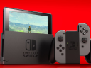 A Nintendo Switch with grey Joy-Cons on a red background. The Legend of Zelda: Breath of the Wild can be seen on the screen via Nintendo