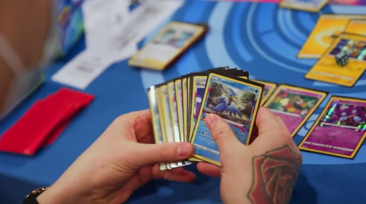 A player looks at his Pokémon Trading Cards, with a Cramorant card, and a rose tattoo on the back of their hand via TCG Day 1 | 2023 Pokémon Charlotte Regional Championships, PokemonTCG Twitch