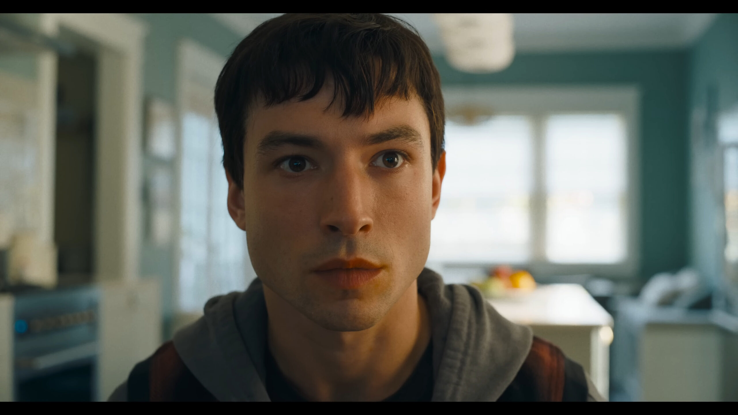 Barry Allen (Ezra Miller) catches a glimpse of his past self in Batman (Michael Keaton) reveals his cache of Batsuits in The Flash (2023), Warner Bros. Pictures