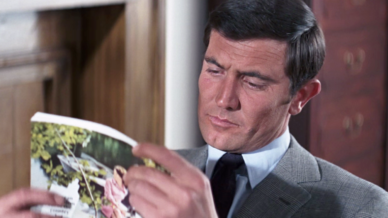 James Bond (George Lazenby) finds some light reading to pass the time in On Her Majesty's Secret Service (1969), United Artists