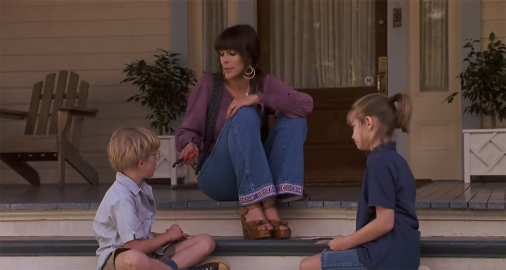 A woman and two kids sit on the steps of a porch.
