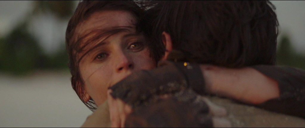 Jyn (Felicity Jones) and Andor (Diego Luna) embrace as Scarif is obliterated in Rogue One: A Star Wars Story (2016), Disney